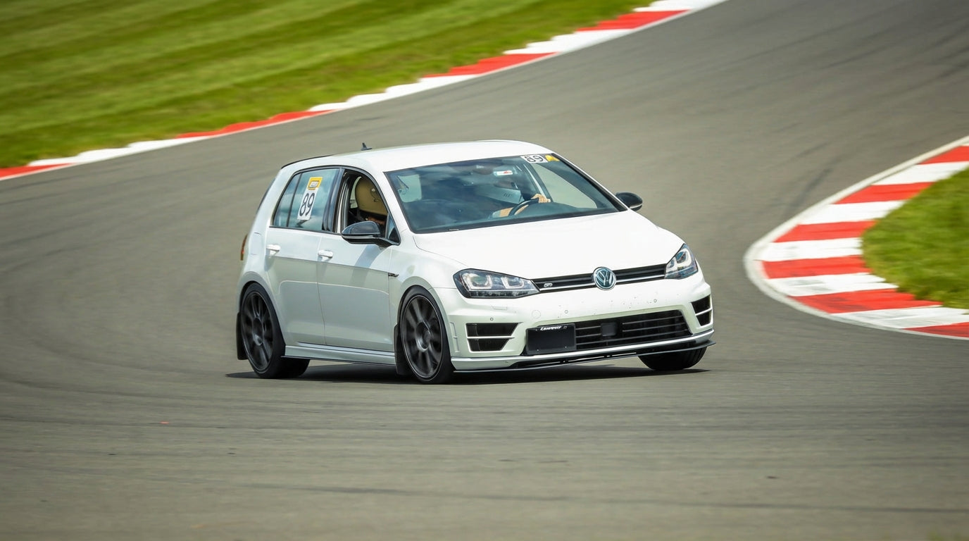 White Volkswagen car on a race track with red and white curbs.